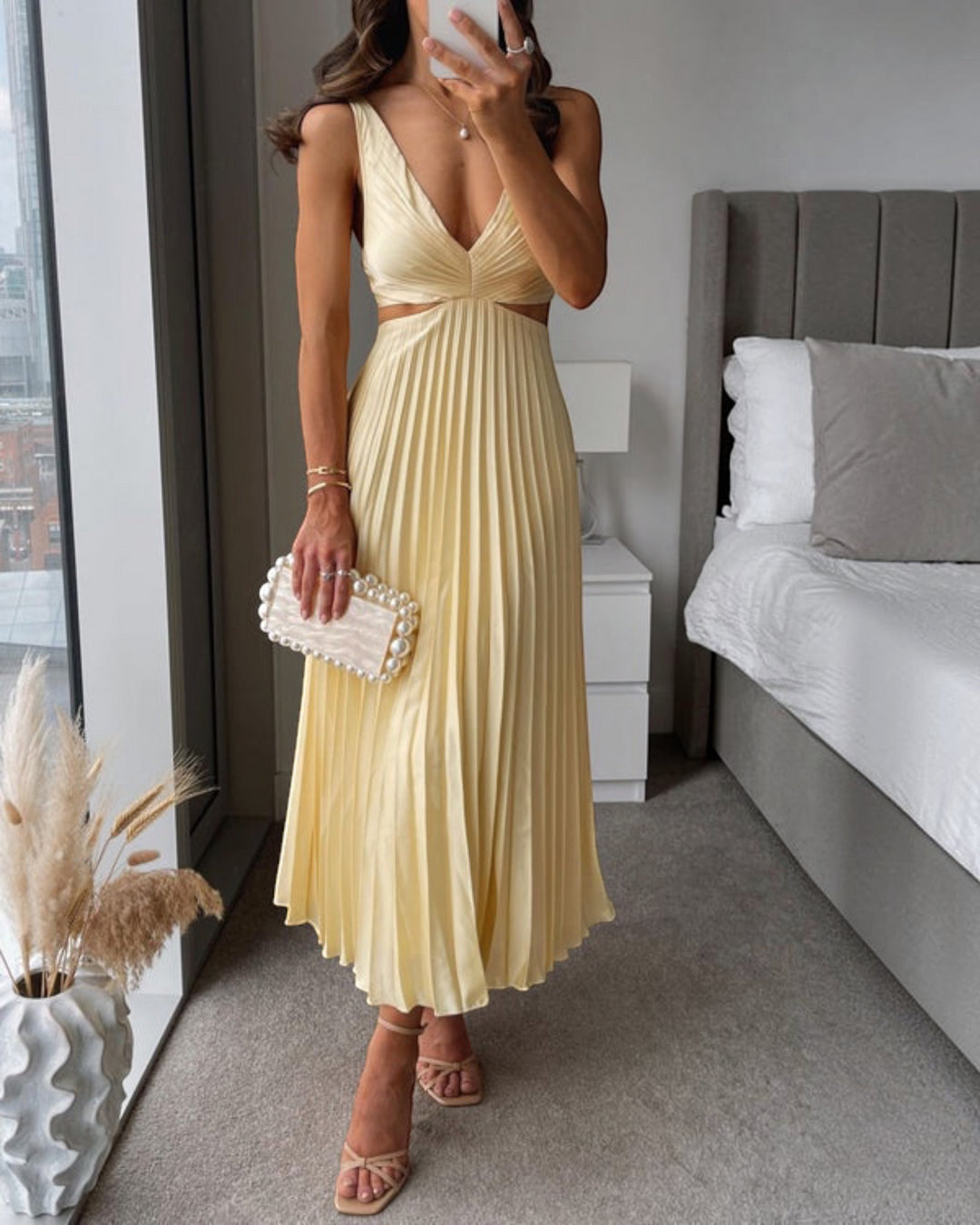 Luna Moda Abito Bellezza yellow pleated maxi dress with cut-out waist, worn with a pearl clutch and strappy sandals.