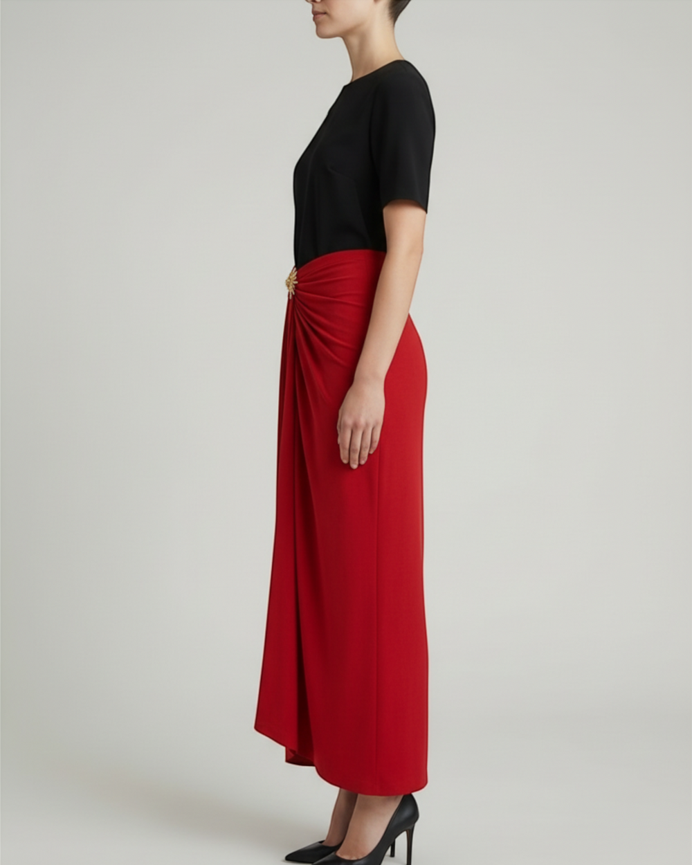 Luna Moda Cleo red midi skirt with side draping and gold sun brooch worn by a model in profile view