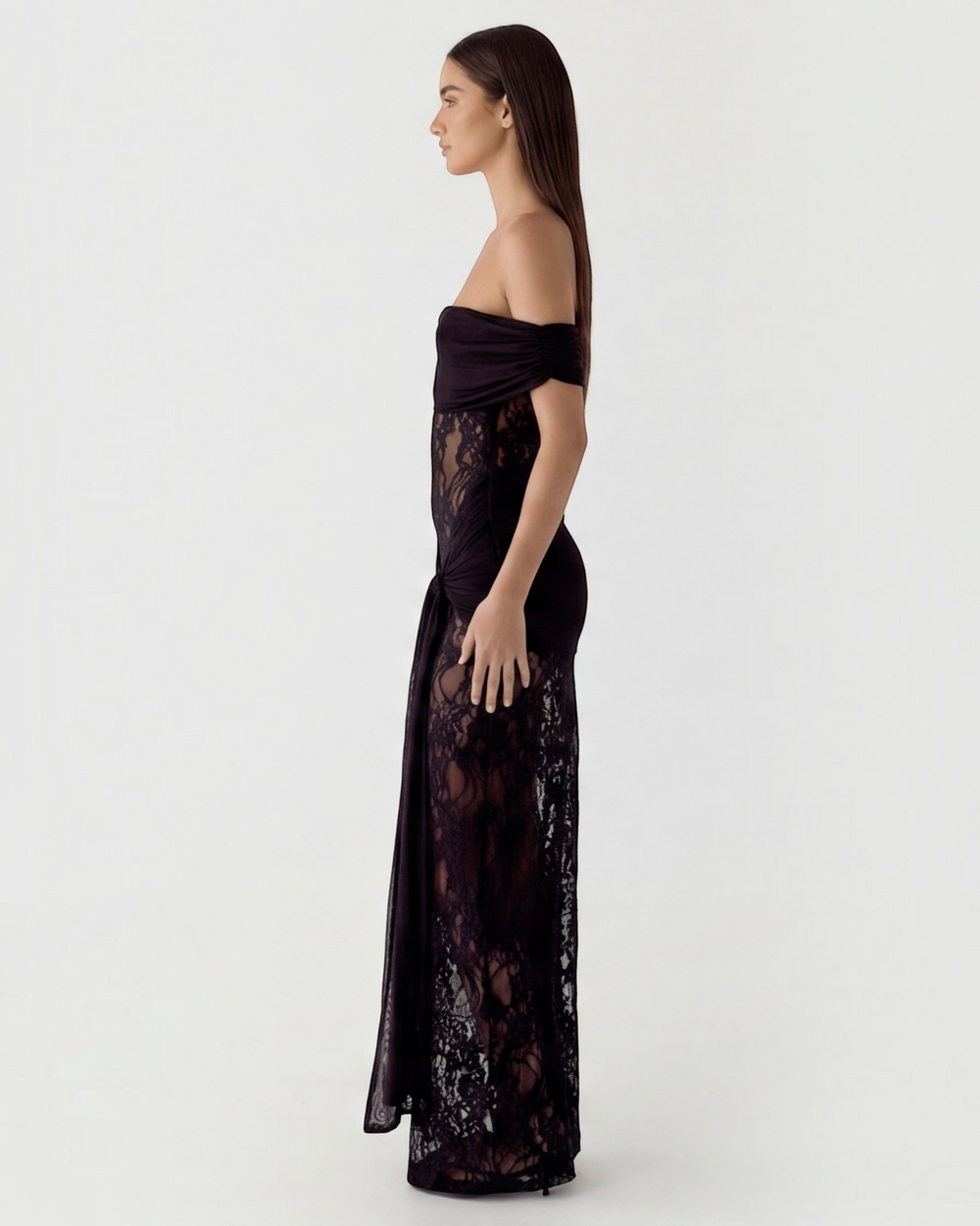 Luna Moda black off-the-shoulder maxi dress with sheer lace panels and draped waist detail on a model, side view.