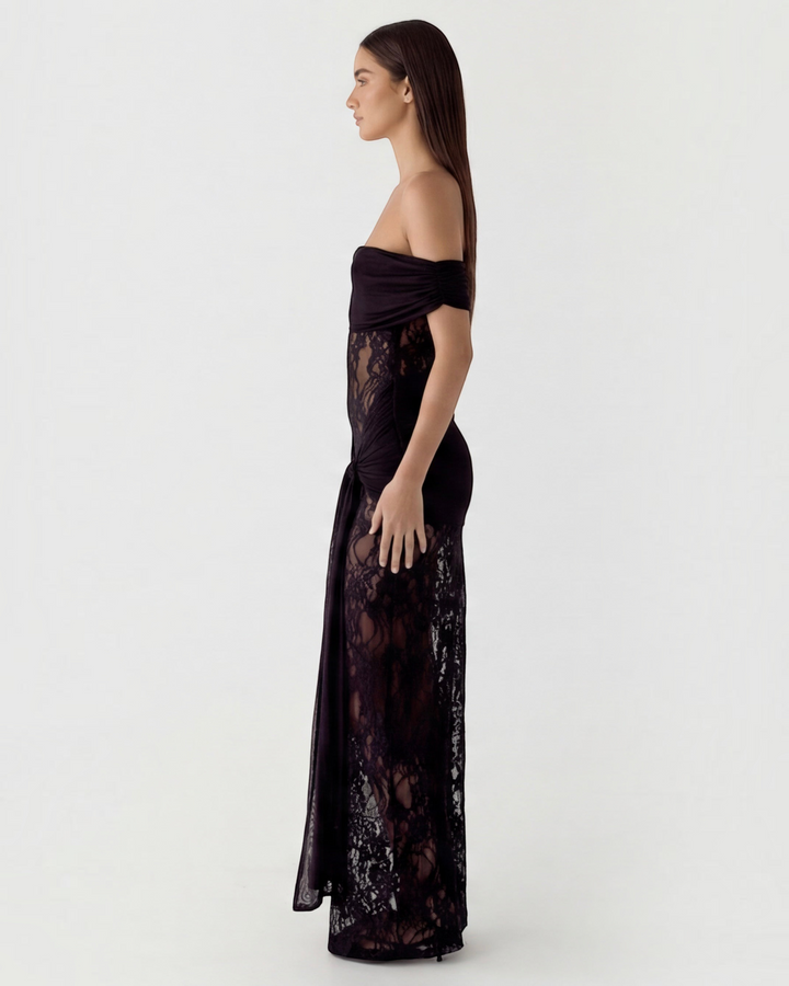 Luna Moda black off-the-shoulder maxi dress with sheer lace panels and draped waist detail on a model, side view.