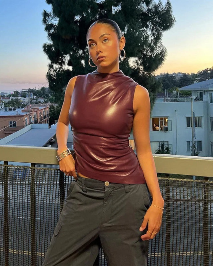 Model wearing a Luna Moda sleeveless burgundy faux leather top with a high neckline in an urban outdoor setting.