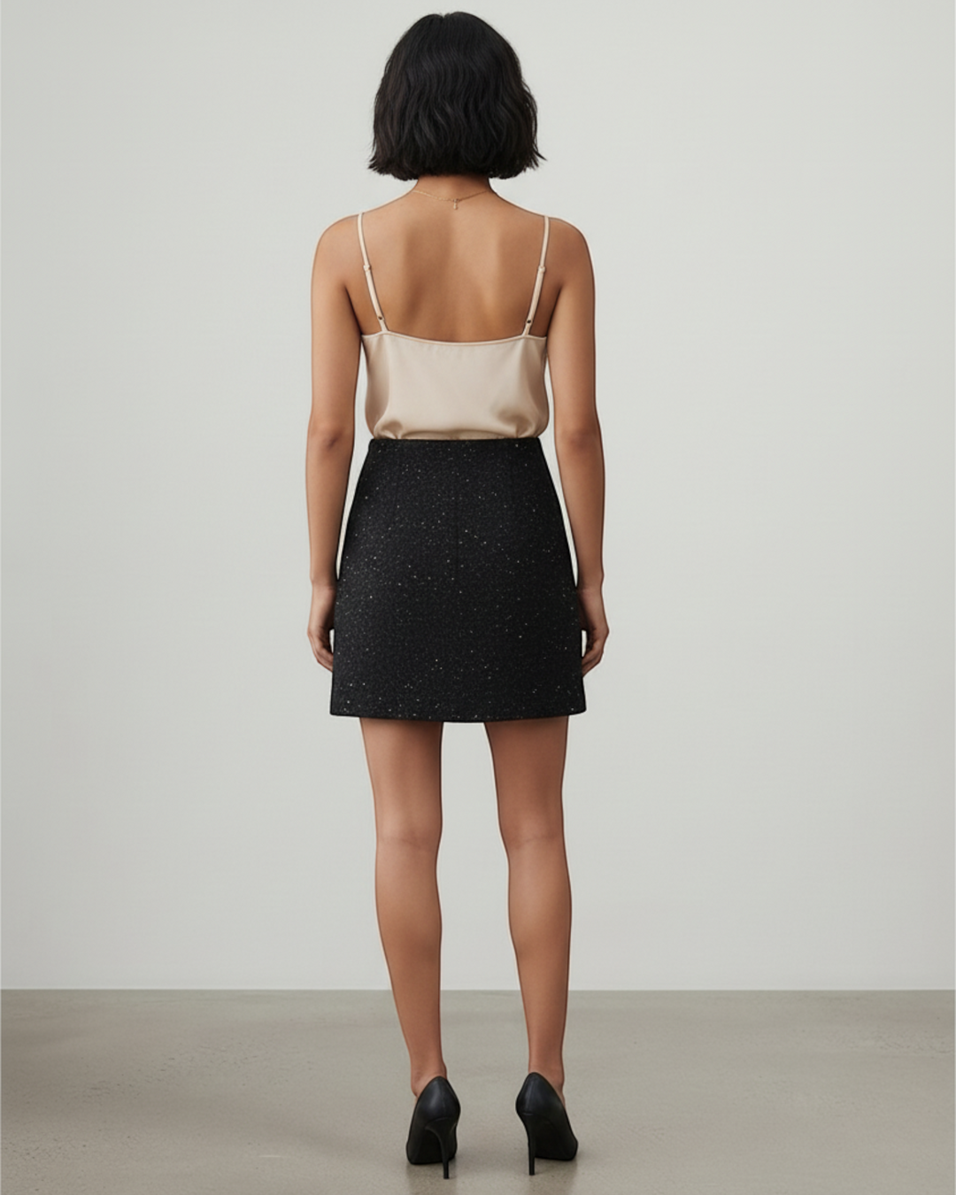 Luna Moda Tasha black textured mini skirt with subtle shimmer, back view on a model wearing a beige camisole