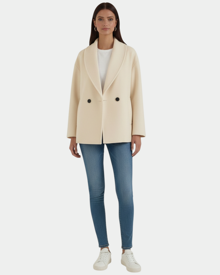 Model wearing a Luna Moda cream oversized double-breasted coat with wide lapels, paired with blue jeans and sneakers.