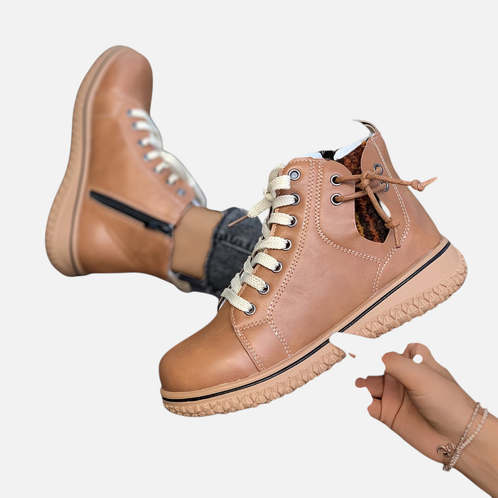 Luna Moda EDUARDA tan leather ankle boots with cream laces and side zipper, held by a hand against a grey background.