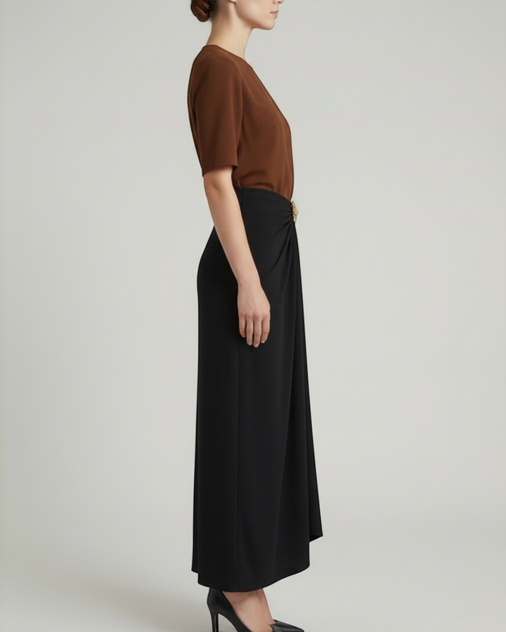 Luna Moda Cleo midi skirt in black with side draping and a gold sun-shaped brooch, worn with a brown top