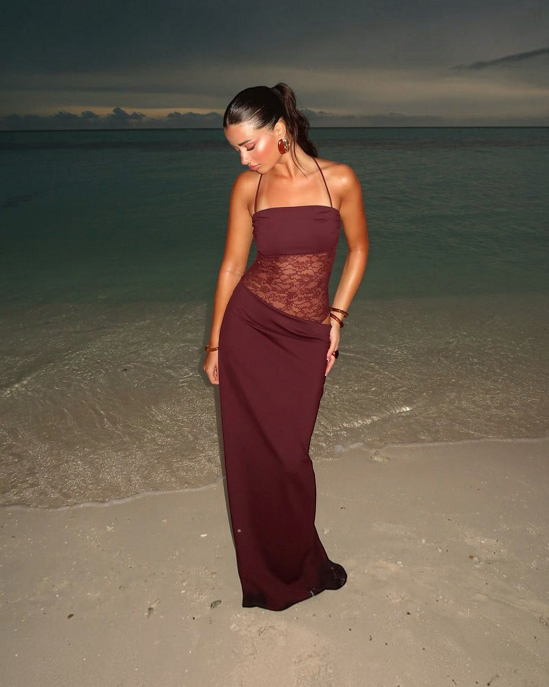 Luna Moda Giulia burgundy velvet maxi dress with mesh lace waist detail worn by a model on a beach at sunset