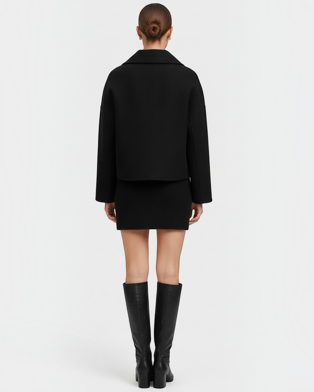 Luna Moda Francesca black double-breasted mid-season coat worn by a model, back view with skirt and knee-high boots.
