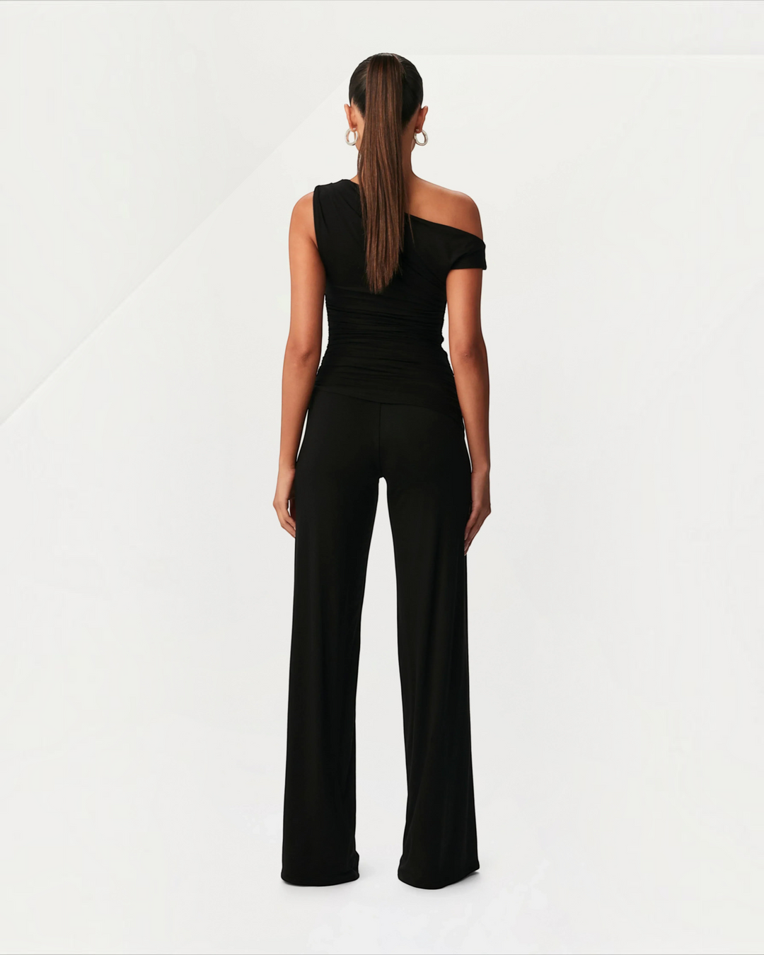Luna Moda black asymmetric two-piece set with side ruching worn by a model, back view.