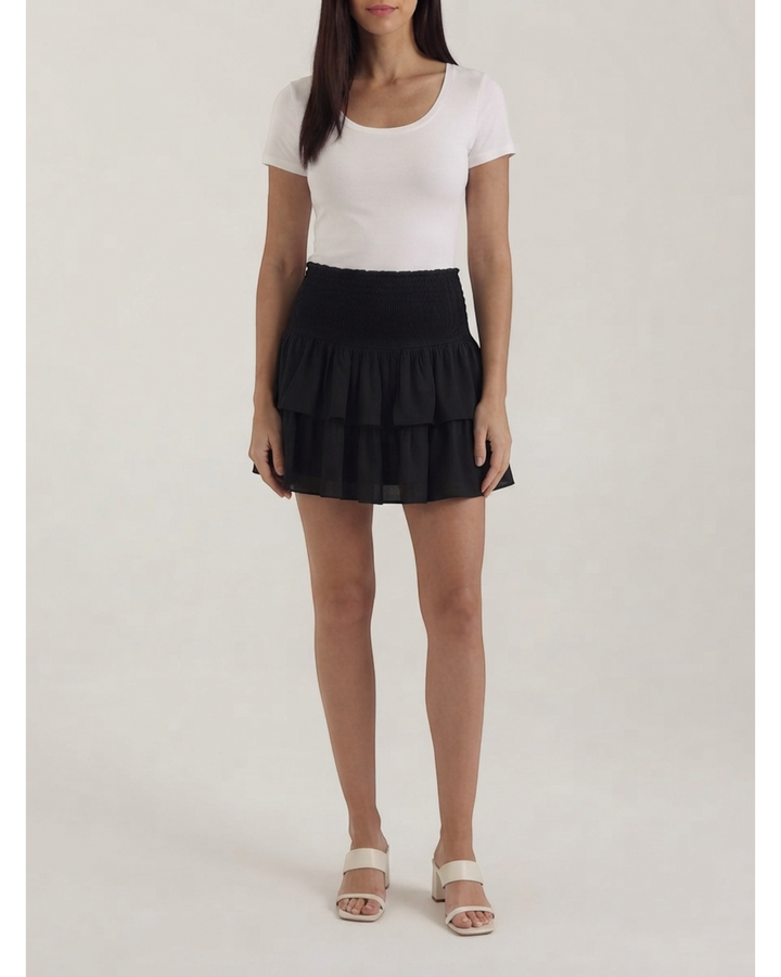 Luna Moda black mini skirt with a smocked high waist and layered ruffles worn by a woman with a white t-shirt