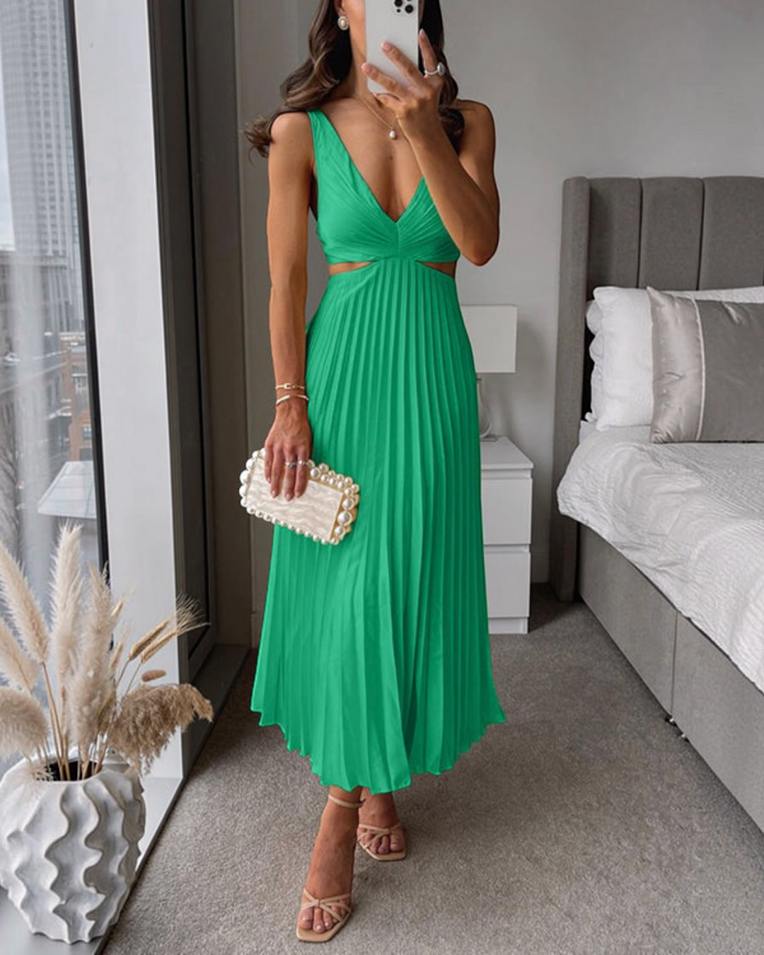 Luna Moda green pleated maxi dress with cut-out waist, worn by a woman with a pearl clutch and heels in a bedroom.