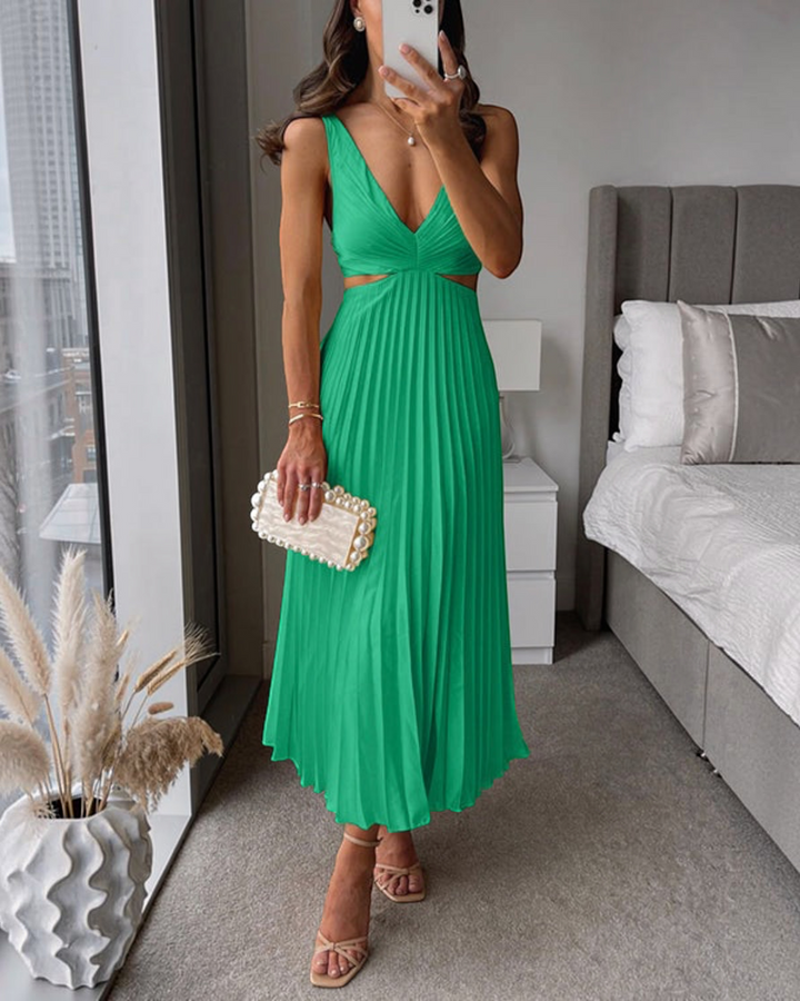 Luna Moda green pleated maxi dress with cut-out waist, worn by a woman with a pearl clutch and heels in a bedroom.