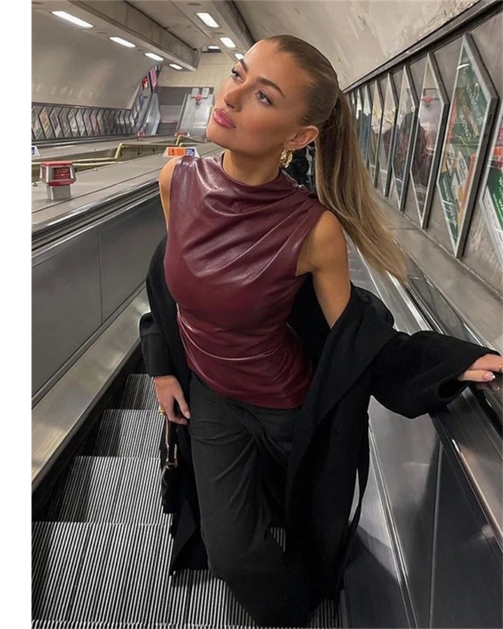 Luna Moda sleeveless burgundy faux leather top with a high neck, worn by a woman on an escalator in a city setting.