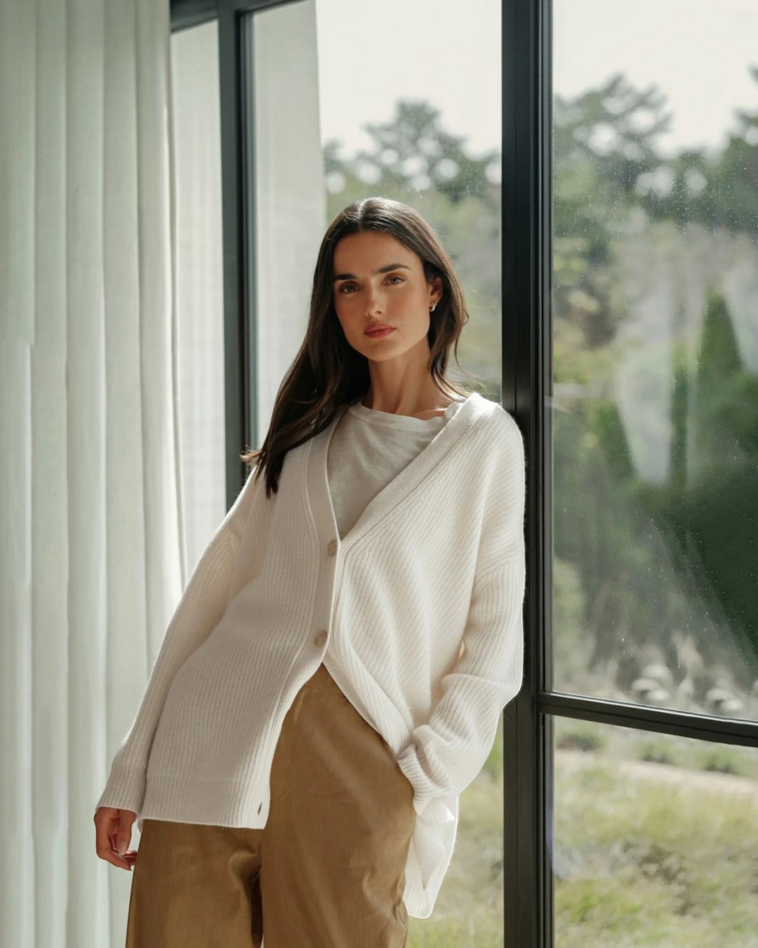 Luna Moda Laura white V-neck cashmere cardigan worn by a woman leaning against a window