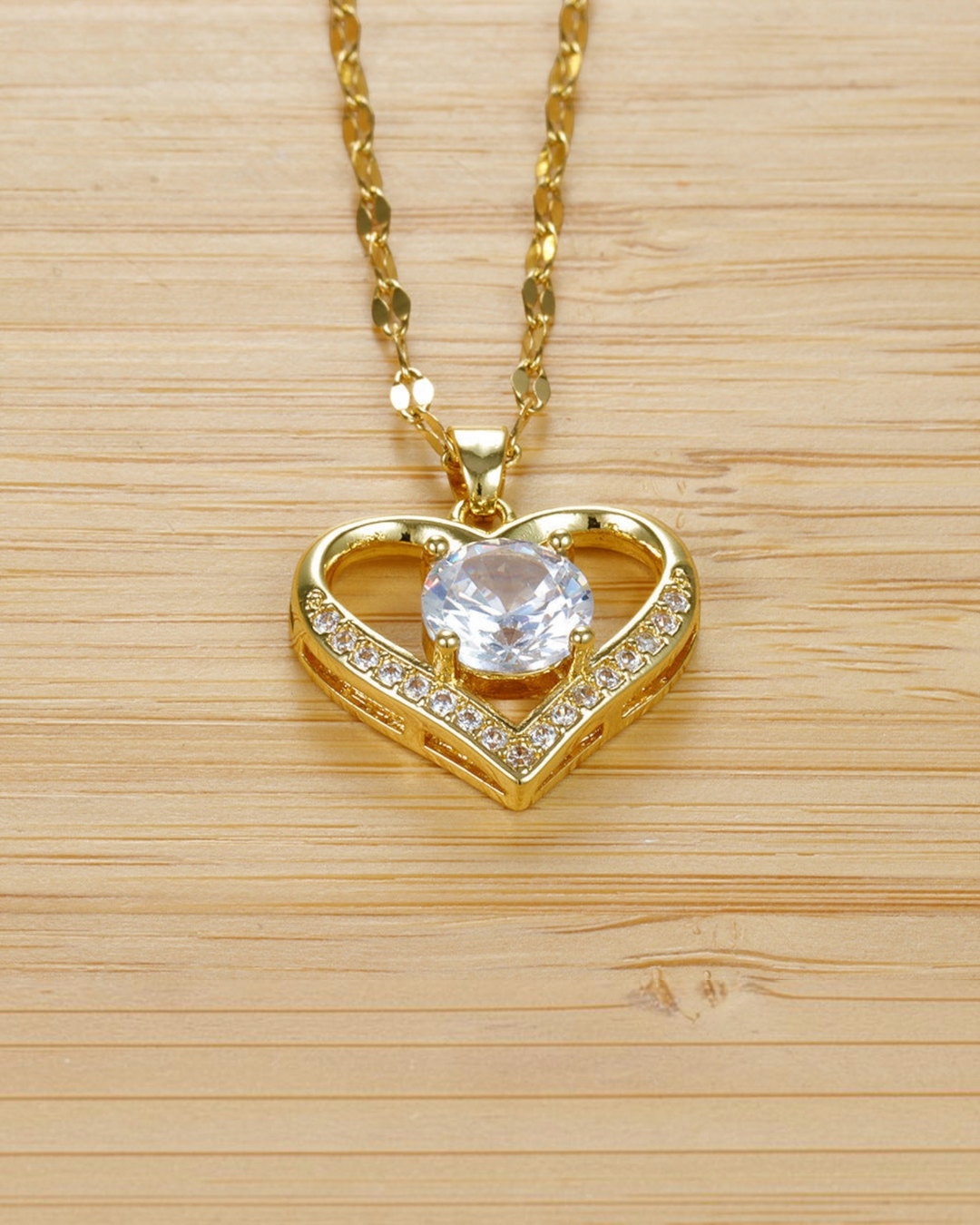 Luna Moda gold heart necklace with a central cubic zirconia stone and side diamonds on a wooden background.