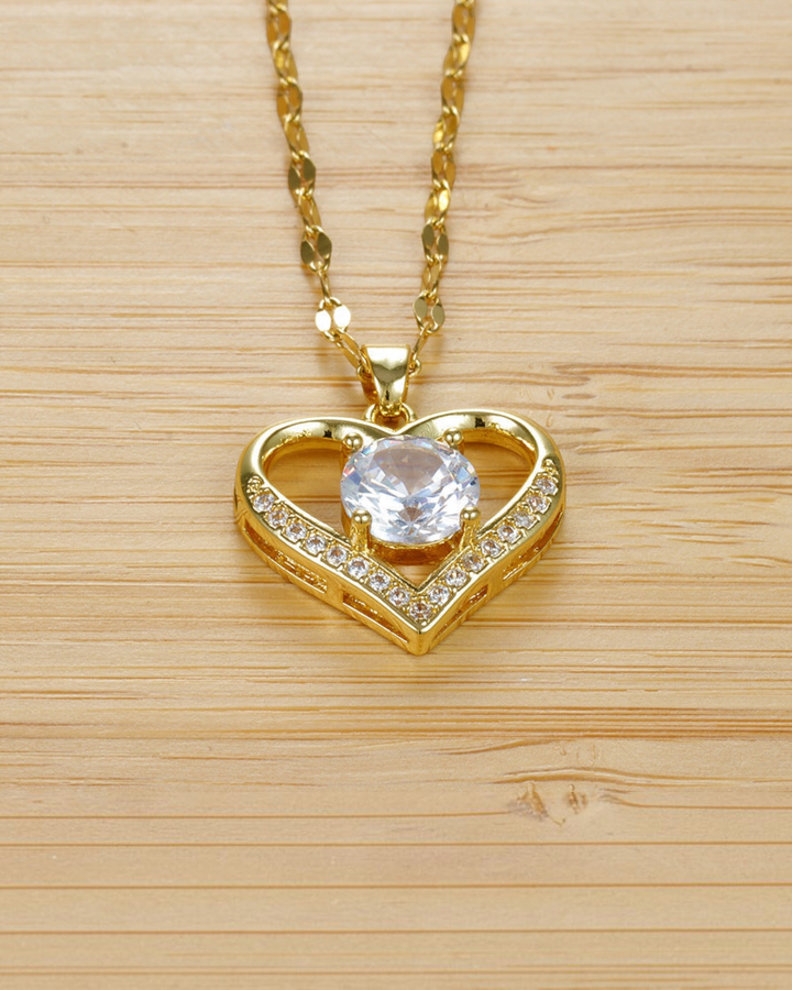 Luna Moda gold heart necklace with a central cubic zirconia stone and side diamonds on a wooden background.
