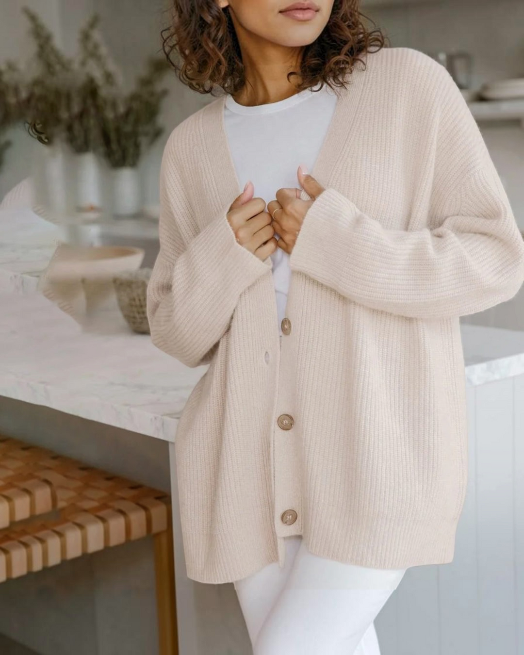 Luna Moda beige cashmere V-neck cardigan with button front, worn over a white top in a bright kitchen setting.