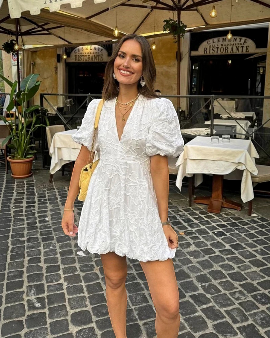 Luna Moda white mini dress with puff sleeves and delicate embroidery worn by a smiling woman at an outdoor cafe