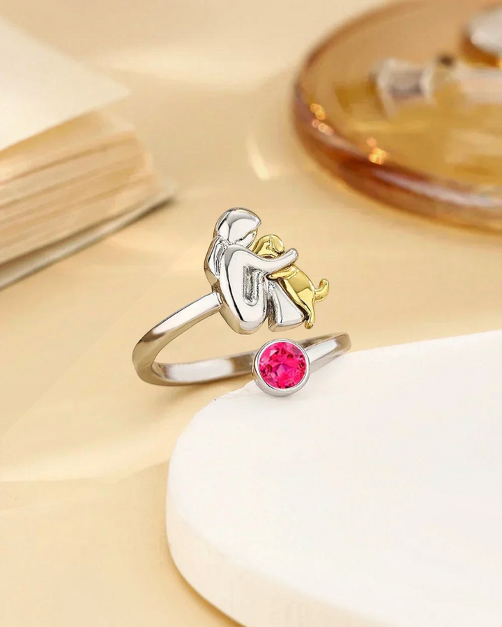 Luna Moda ring featuring a silver person hugging a gold dog with a vibrant pink crystal accent
