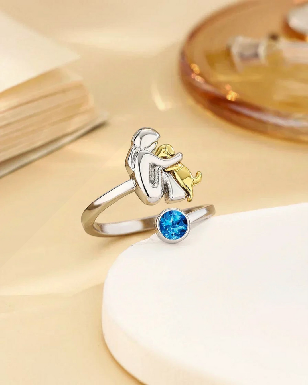Luna Moda ring featuring a silver human and gold dog embrace with a sparkling blue crystal accent.