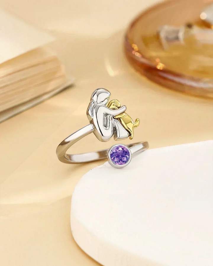 Luna Moda ring featuring a silver human and gold dog embrace design with a purple crystal accent
