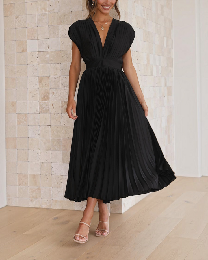 Luna Moda Isla black pleated midi dress with deep V-neck and high waist, worn by a model against a stone wall.