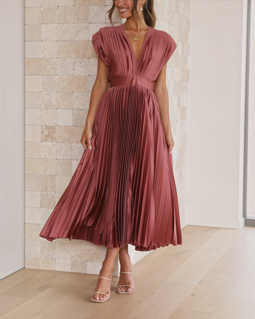 Luna Moda Isla rose red pleated midi dress with a deep V-neckline and high waist, worn by a woman in a bright room.