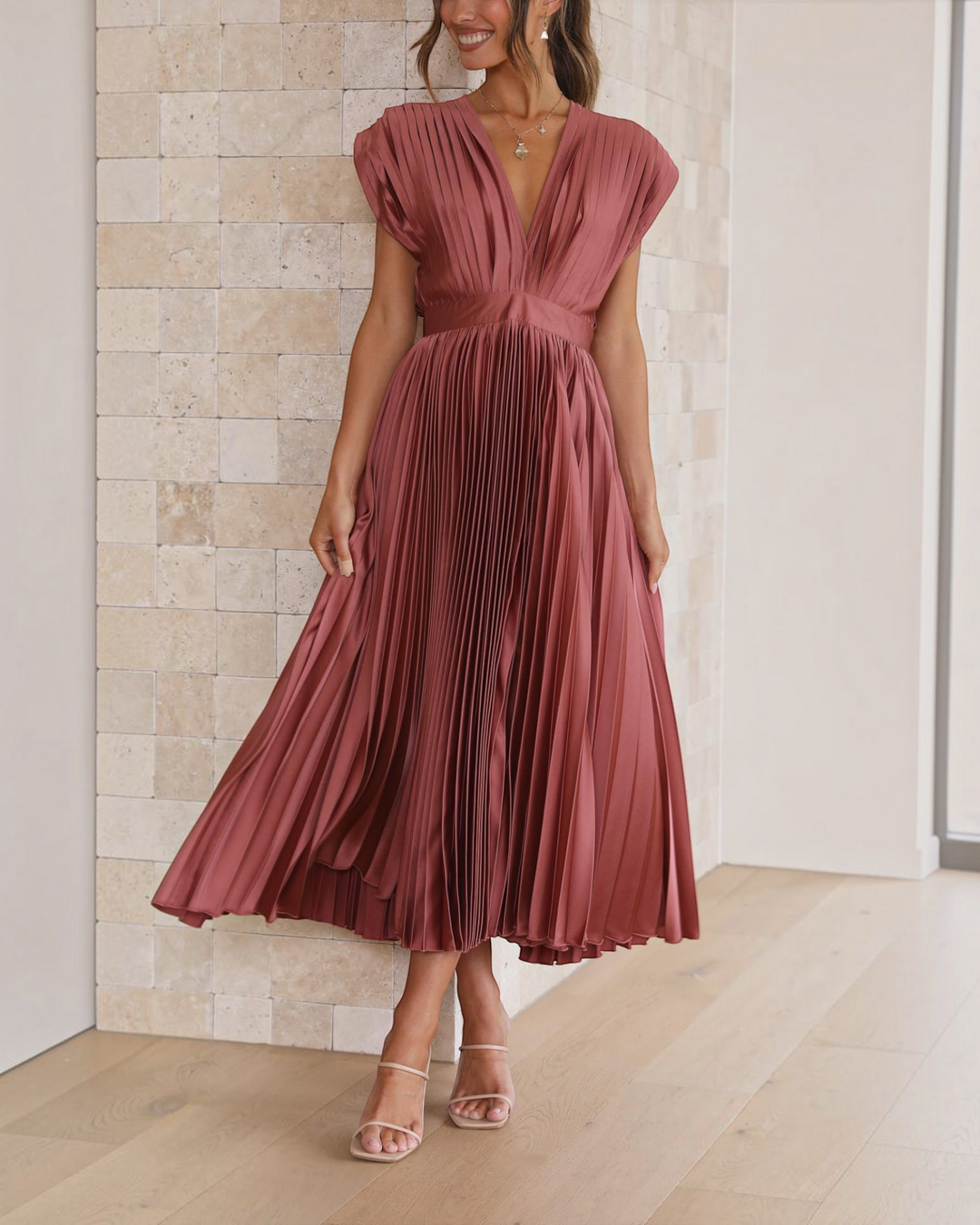 Luna Moda Isla rose red pleated midi dress with a deep V-neckline and high waist, worn by a woman in a bright room.