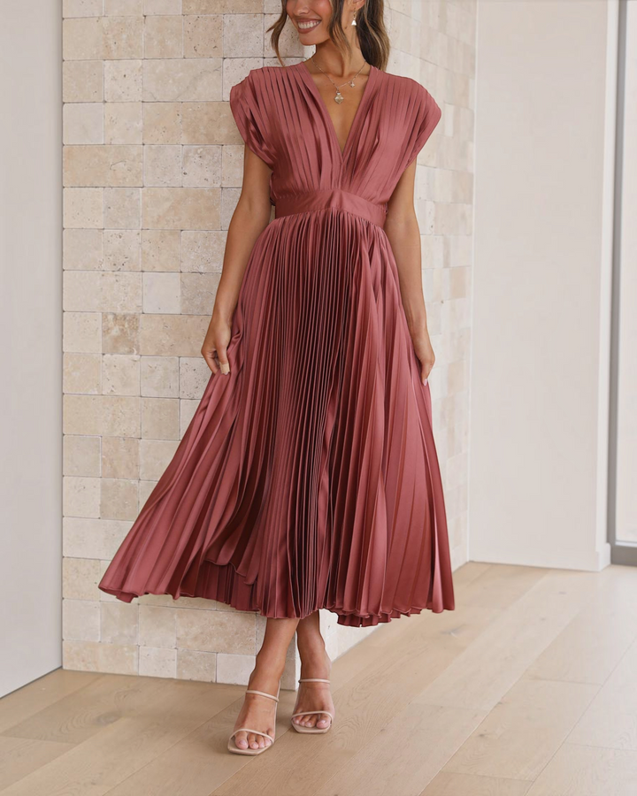 Luna Moda Isla rose red pleated midi dress with a deep V-neckline and high waist, worn by a woman in a bright room.