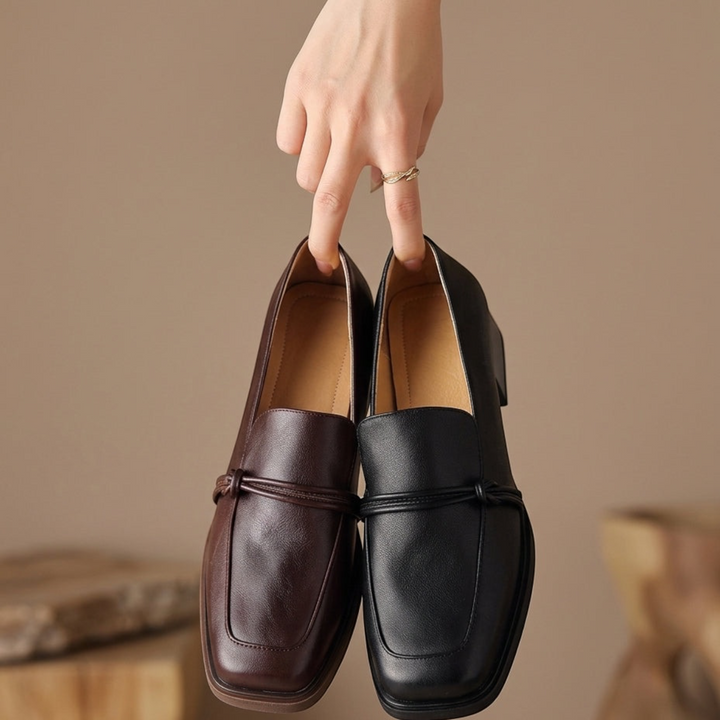 Luna Moda Aurea block heel loafers in black and brown leather with decorative bow detail held by hand
