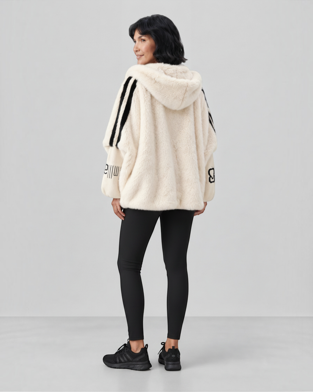 Luna Moda cream faux fur hooded jacket with black striped sleeves and decorative text worn by a woman from behind