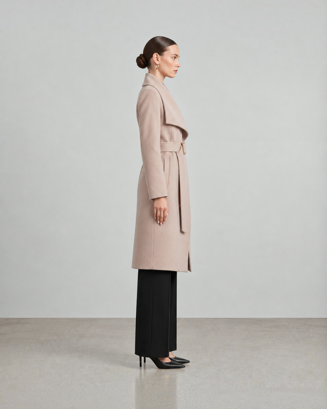Luna Moda beige long belted coat worn by a model in profile view, featuring a shawl collar and tailored silhouette.