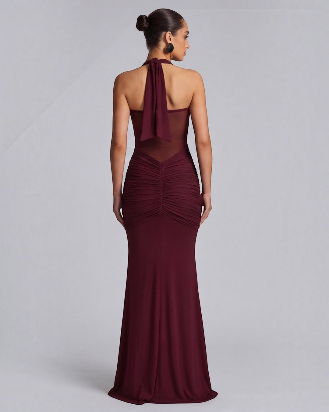 Luna Moda wine red mermaid gown with mesh waist detail and ruched hips worn by a model in a back view