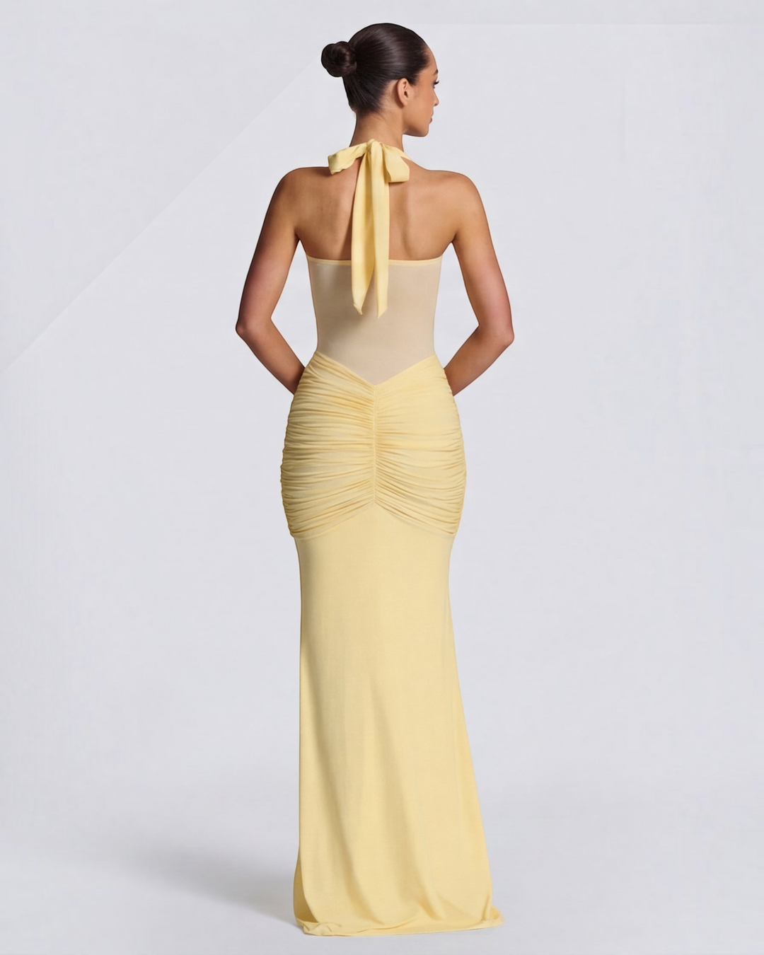 Luna Moda yellow mermaid gown with mesh waist detail, ruched hips, and halter neck tie, back view on model.