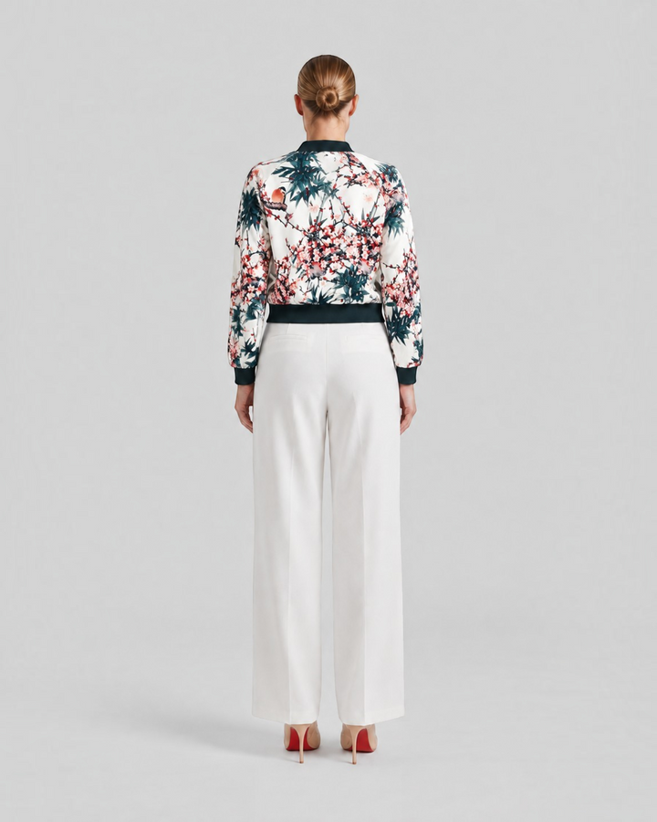 Luna Moda Arianna bomber jacket with vibrant floral print, black ribbed trim, and white wide-leg trousers, back view.