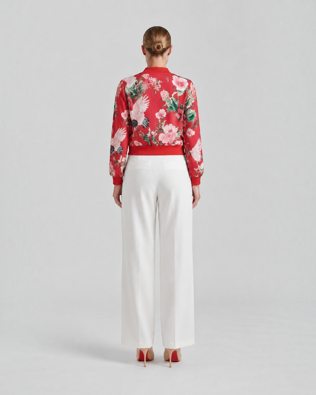 Luna Moda Arianna bomber jacket in red with vibrant floral print and crane motifs, worn with white trousers