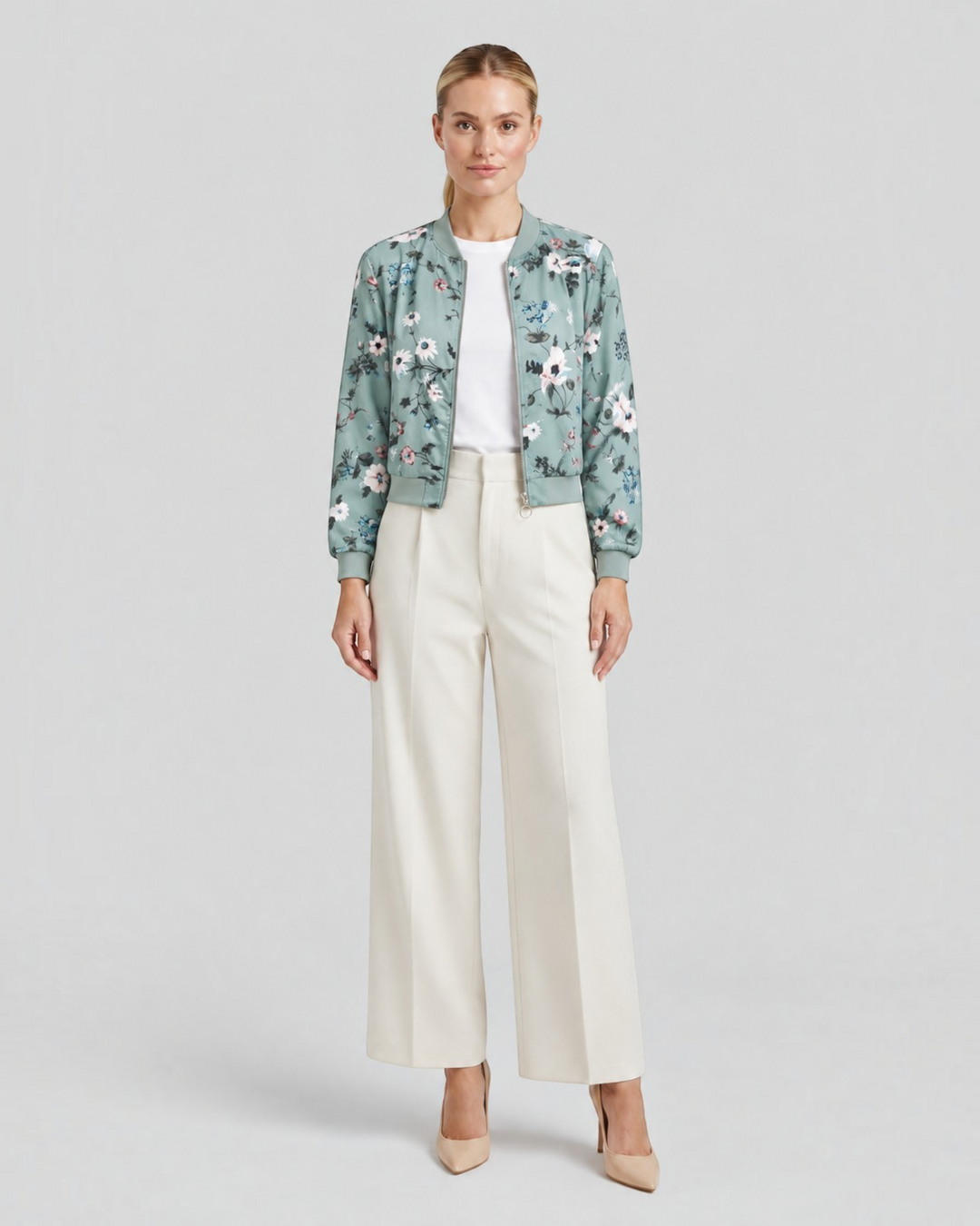 Luna Moda Arianna bomber jacket in sage green with floral print, worn by a model with white trousers and heels.