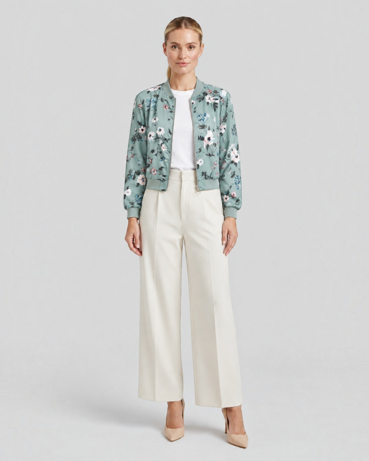 Luna Moda Arianna bomber jacket in sage green with floral print, worn by a model with white trousers and heels.