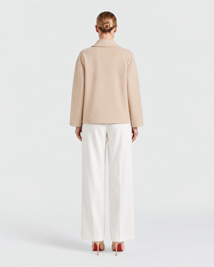 Back view of a model wearing a Luna Moda beige oversized coat with a classic collar and white trousers.
