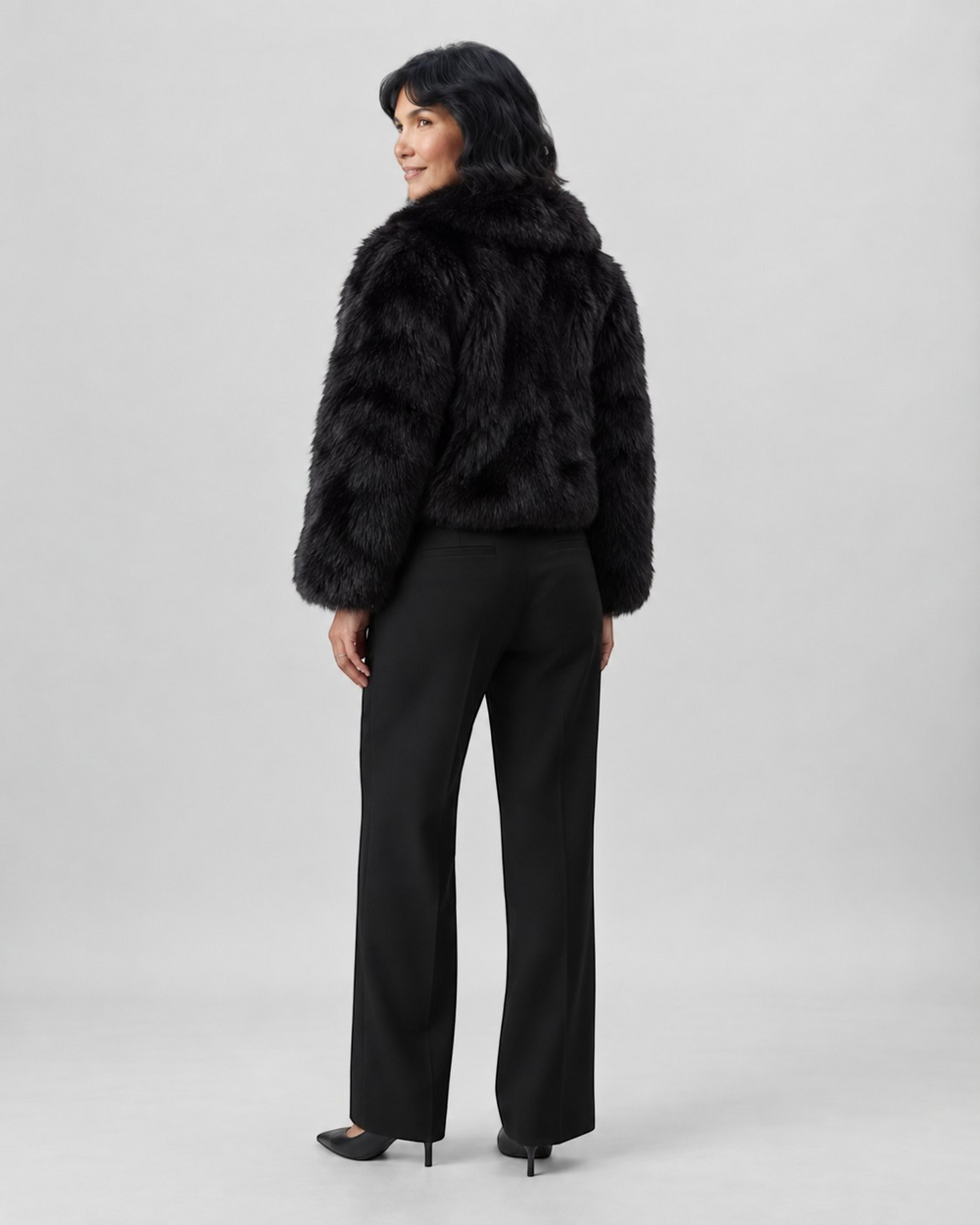 Luna Moda black faux fur coat with wide collar worn by a woman with black trousers and heels, back view