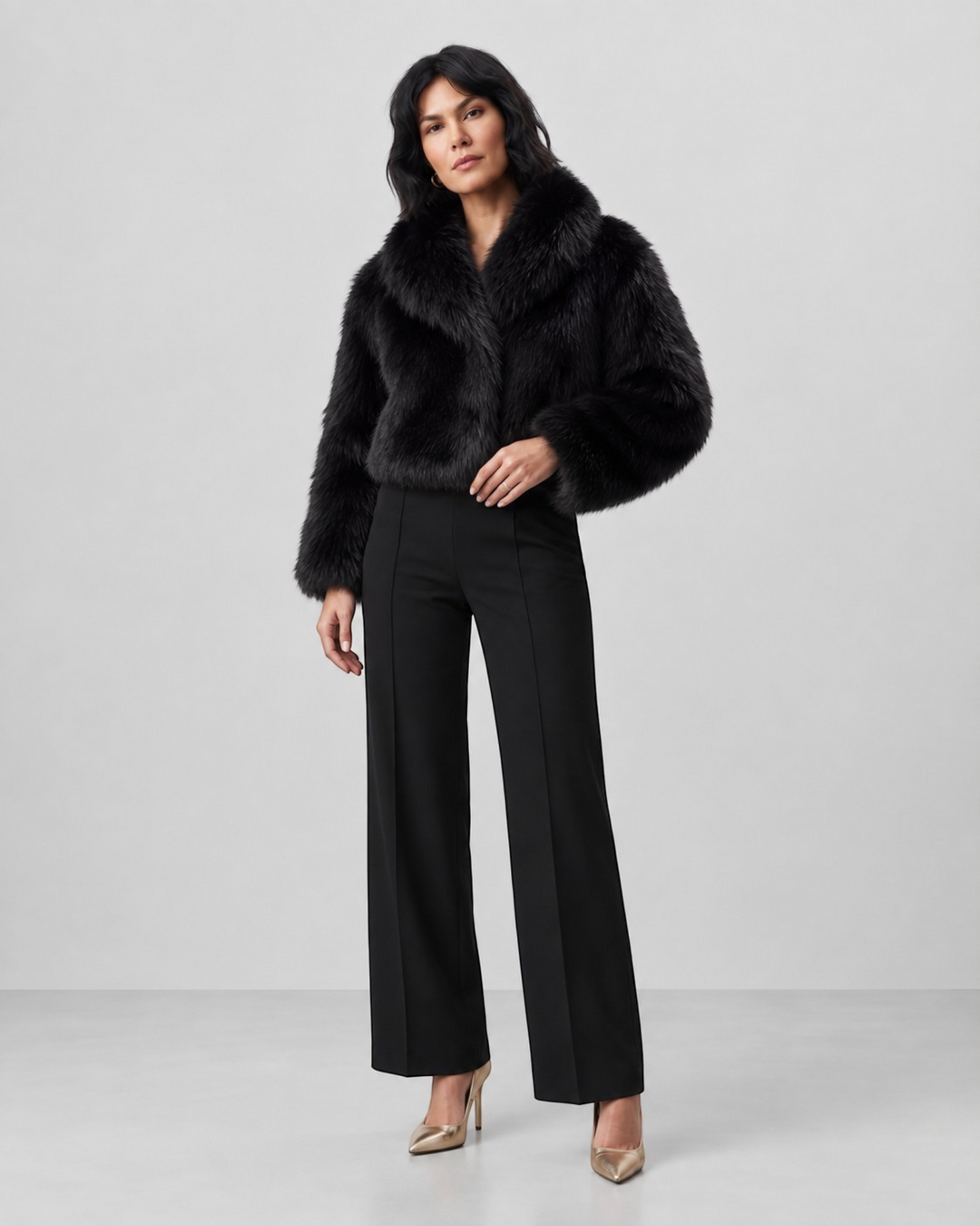 Model wearing a Luna Moda black faux fur cropped coat with a wide collar and long sleeves paired with black trousers