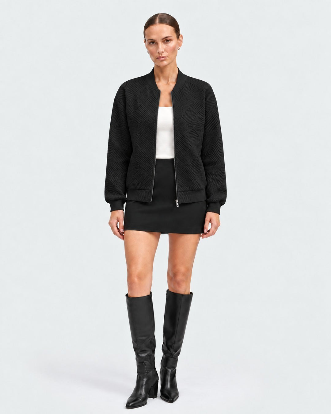 Model wearing a black Luna Moda bomber jacket with a subtle geometric pattern, paired with a skirt and knee-high boots.