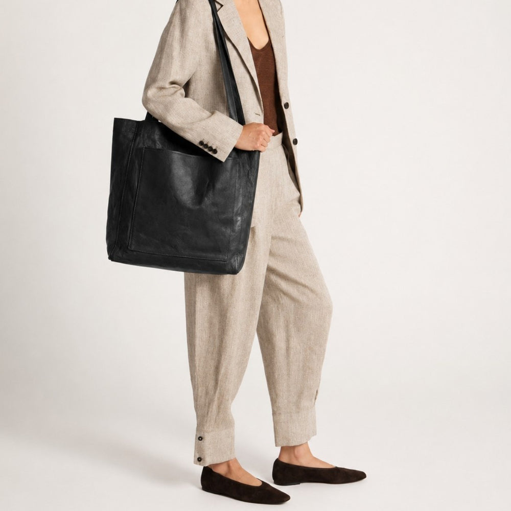 Luna Moda black vintage-effect leather shopper bag worn on the shoulder by a woman in a beige linen suit