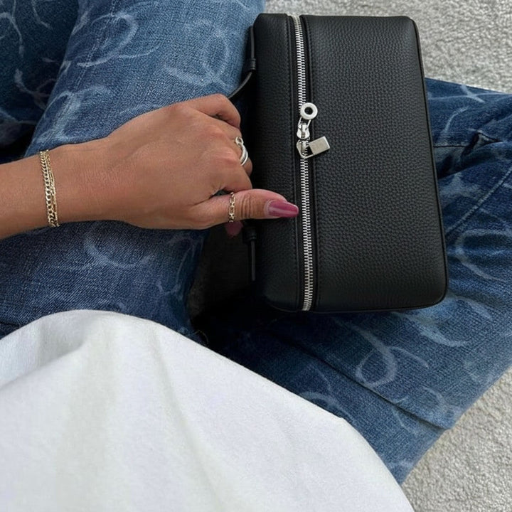 Luna Moda black structured handbag with silver zipper detail held by a woman wearing patterned blue jeans