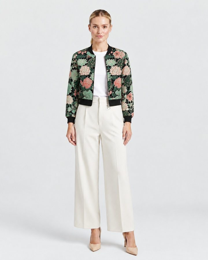 Luna Moda bomber jacket with a black base and vibrant botanical floral print worn by a woman with white trousers.
