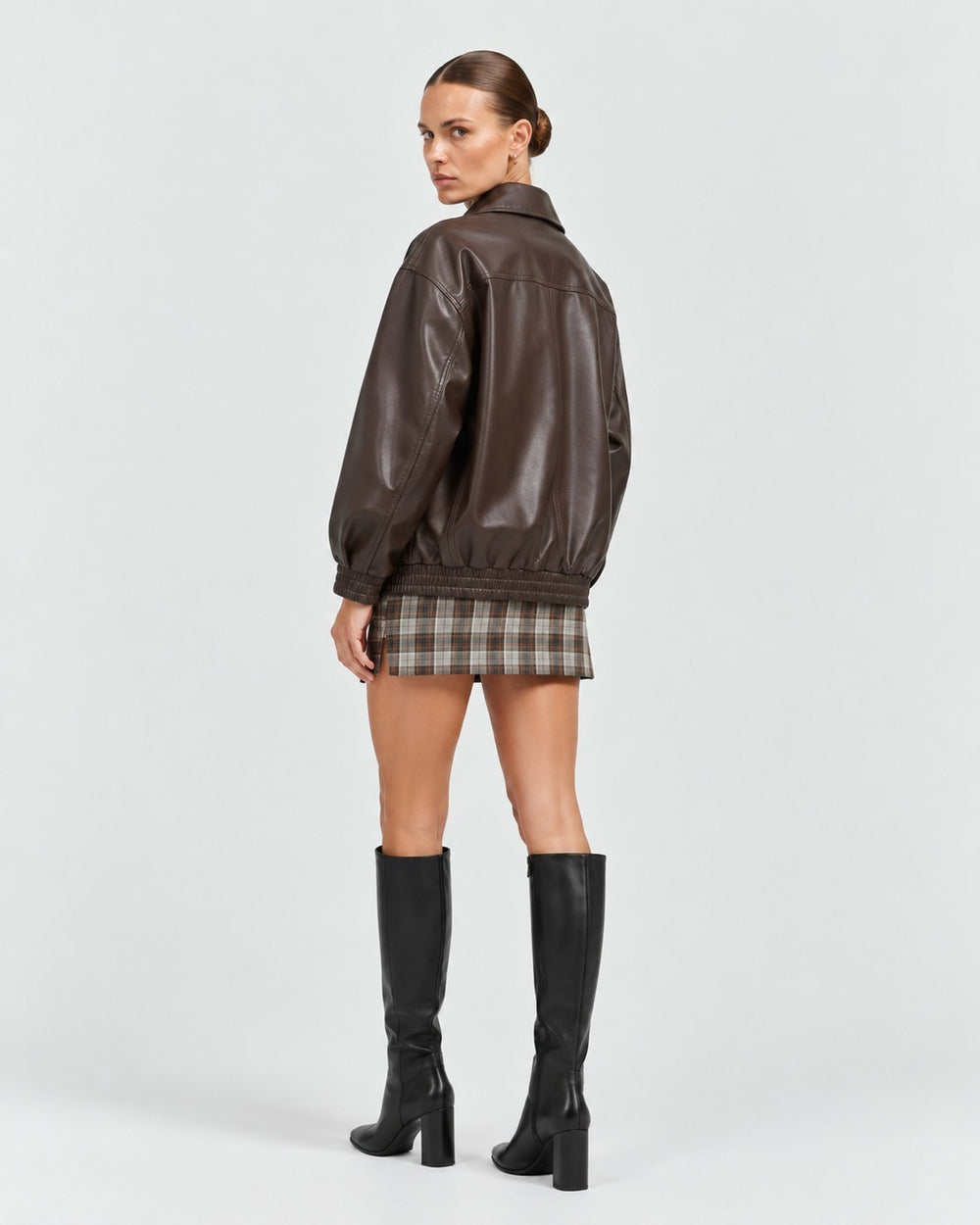 Model wearing a Luna Moda brown faux leather jacket with a relaxed fit, paired with a plaid skirt and black boots.