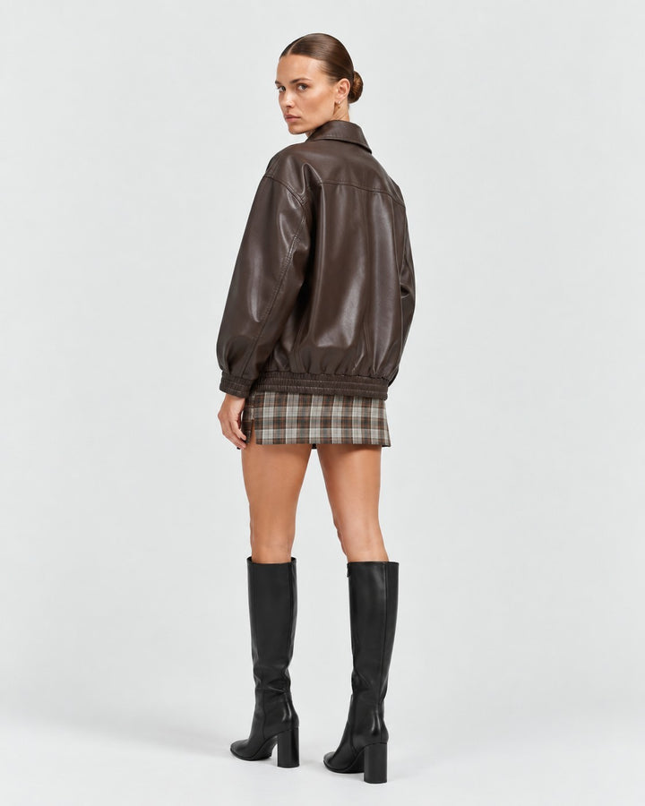 Model wearing a Luna Moda brown faux leather jacket with a relaxed fit, paired with a plaid skirt and black boots.