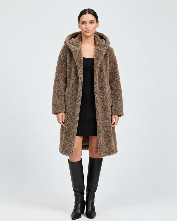 Luna Moda brown knee-length wool teddy coat with a hood, worn by a model over a black dress and tall leather boots.