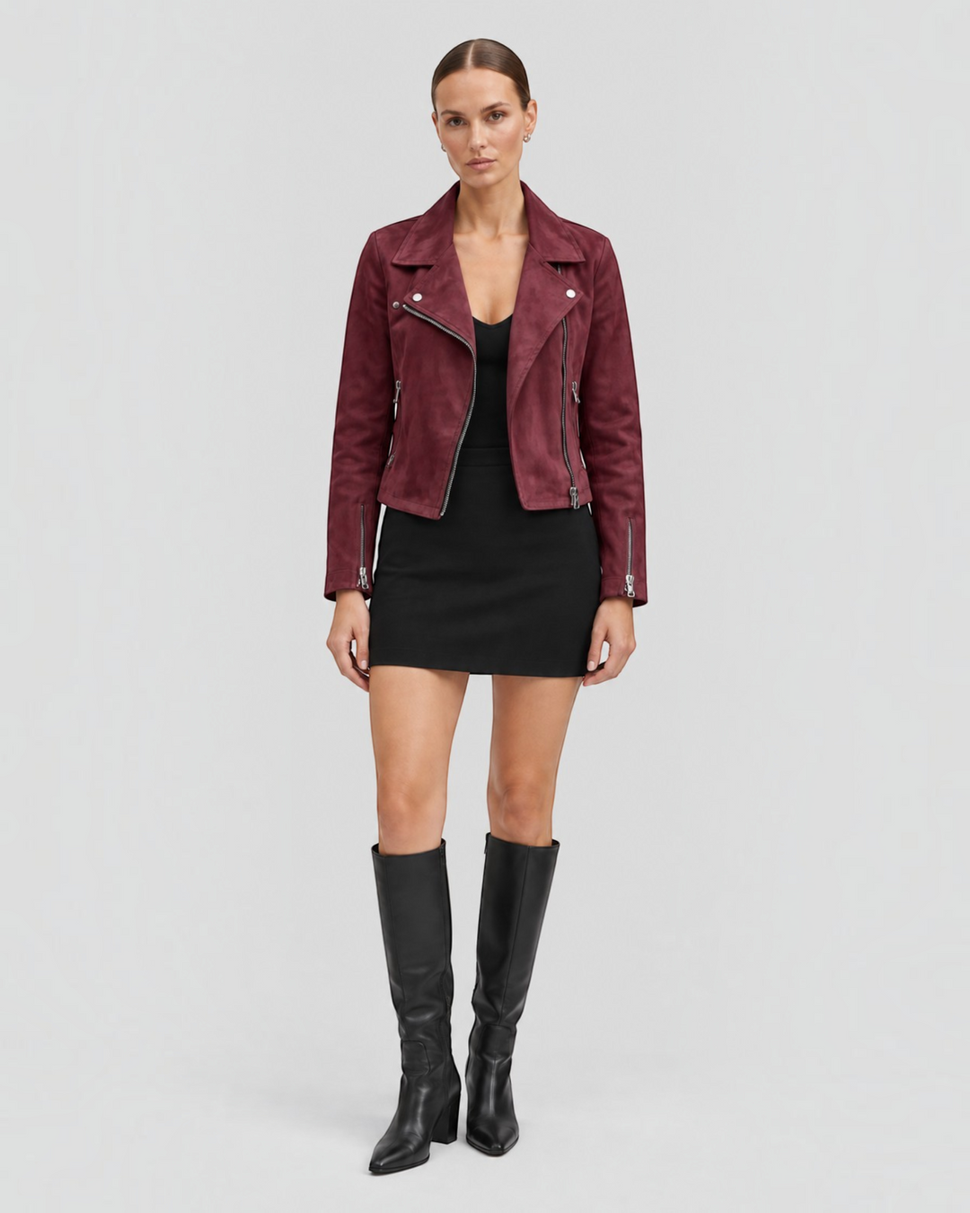 Luna Moda burgundy suede biker jacket with silver zippers worn by a model with a black dress and knee-high boots