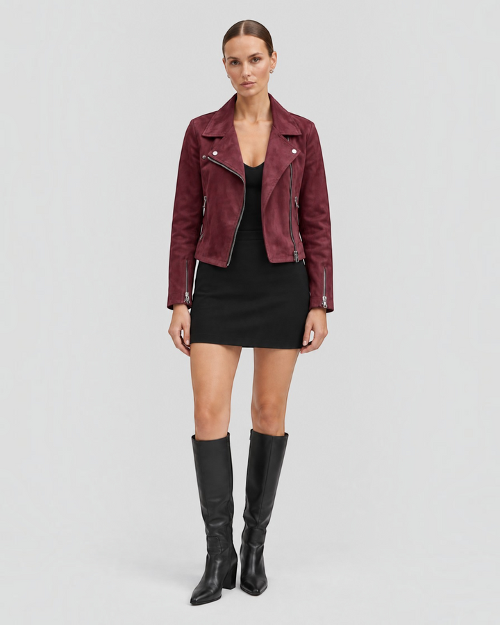 Luna Moda burgundy suede biker jacket with silver zippers worn by a model with a black dress and knee-high boots