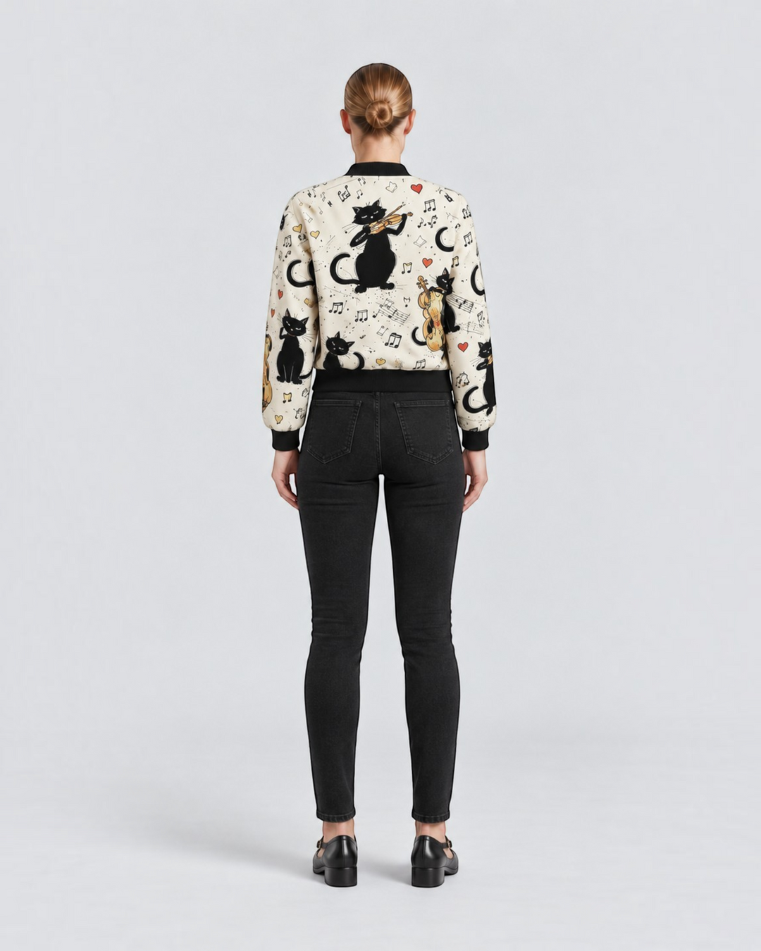 Luna Moda bomber jacket featuring a cream base with black cat and musical instrument print, worn with black jeans.
